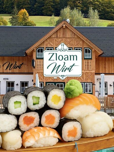 Ein rustikales Restaurant mit dem Namen "Zloam Wirt" in einer malerischen Umgebung. Im Vordergrund liegt eine Sushi-Platte auf einem Holzboot. | © www.zloam.at