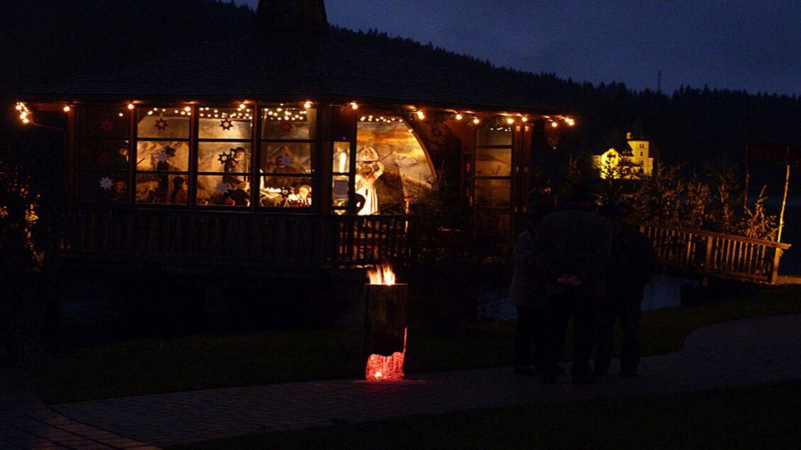 Eine gemütliche Hütte bei Nacht, beleuchtet mit Lichtern. Im Vorgarten stehen mehrere Personen und genießen die Atmosphäre. | © Gemeinde Grundlsee