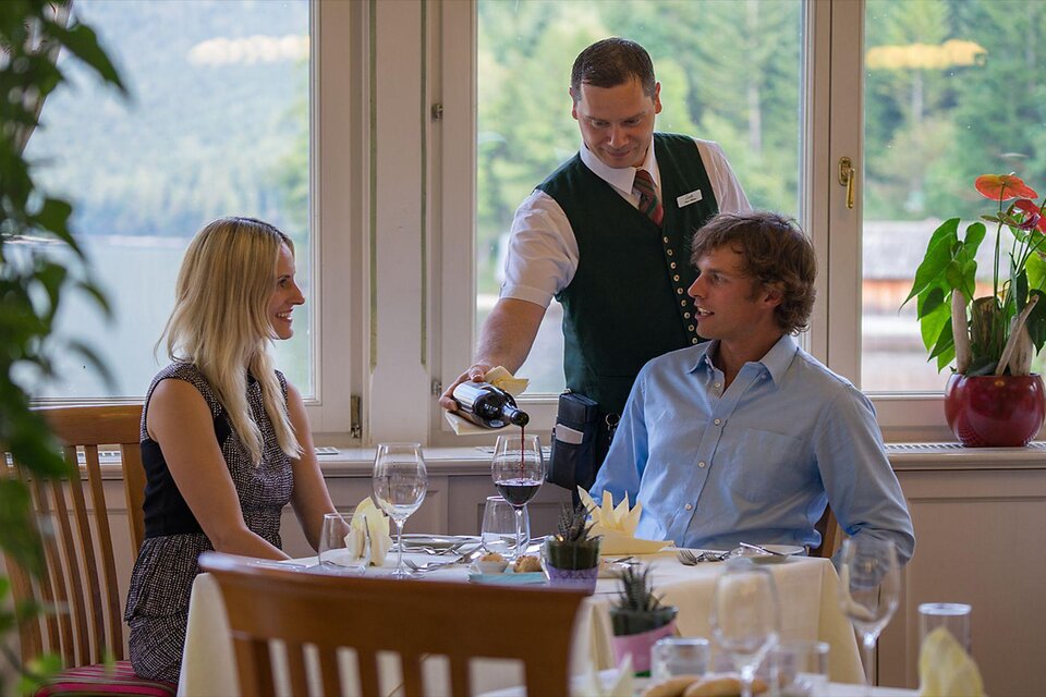 Ein elegantes Restaurant mit einem Kellner, der Wein an ein Paar serviert. Die Gäste sitzen an einem schön gedeckten Tisch mit Blick ins Freie. | © Florian Loitzl