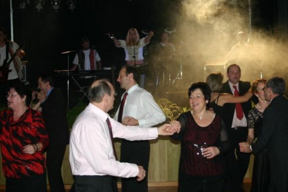 Eine festliche Tanzveranstaltung mit fröhlichen Menschen in eleganter Kleidung. Im Hintergrund spielt eine Band und es gibt ein stimmungsvolles Licht.