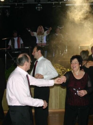 A festive dance event with cheerful people in elegant clothing. A band is playing in the background and there is an atmospheric light.