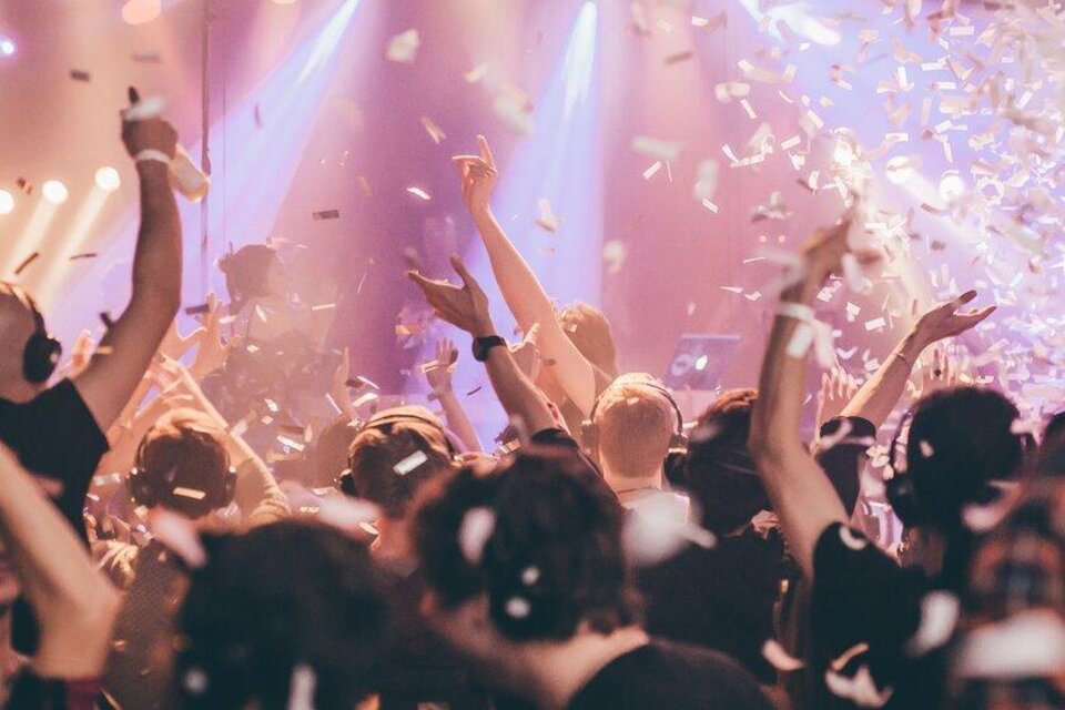 Eine lebhafte Partyszene mit fröhlichen Menschen, die ihre Hände in die Luft heben. Bunte Lichter und Konfetti sorgen für eine festliche Atmosphäre. | © silent-disco-austria