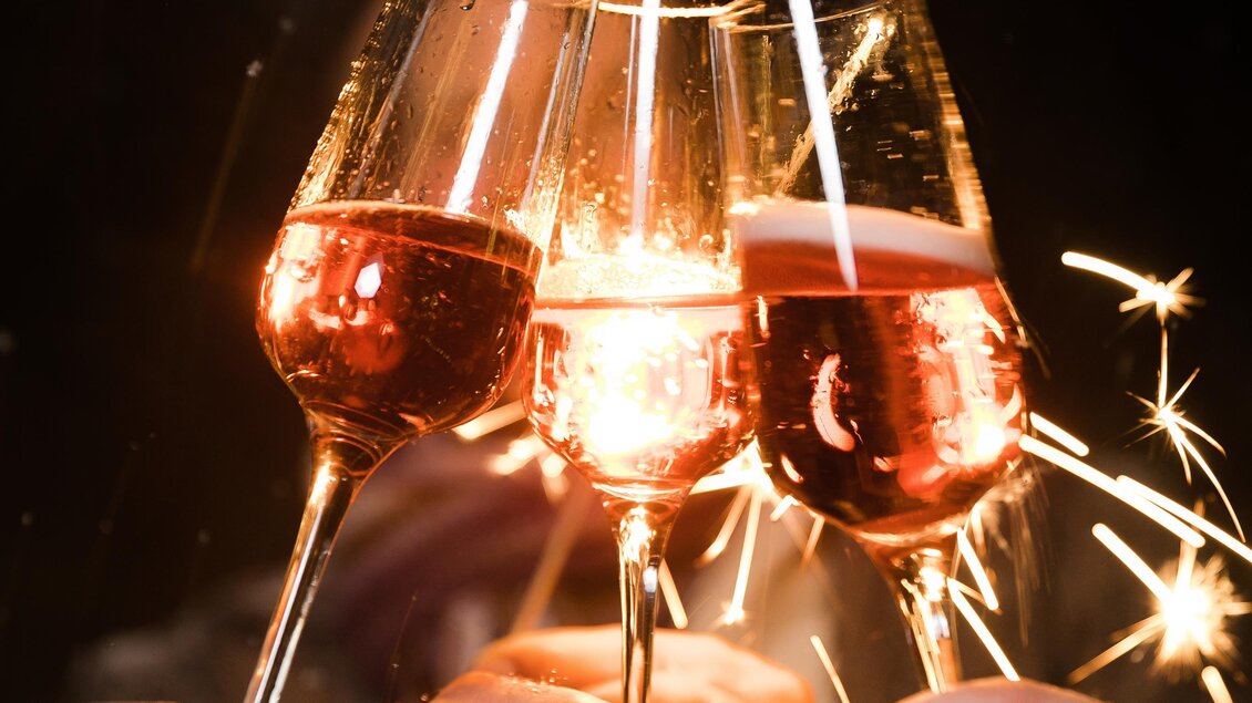 Drei Sektgläser stoßen an und funken sprühen. Es ist eine Feieratmosphäre in der Nacht. | © Achromatic Photography
