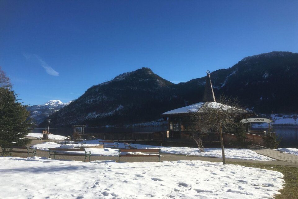 Eine idyllische Winterlandschaft mit schneebedecktem Boden und Bergen im Hintergrund. Im Vordergrund steht ein Holzpavillon neben einer Holzbank. | © Tourismusverband Ausseerland