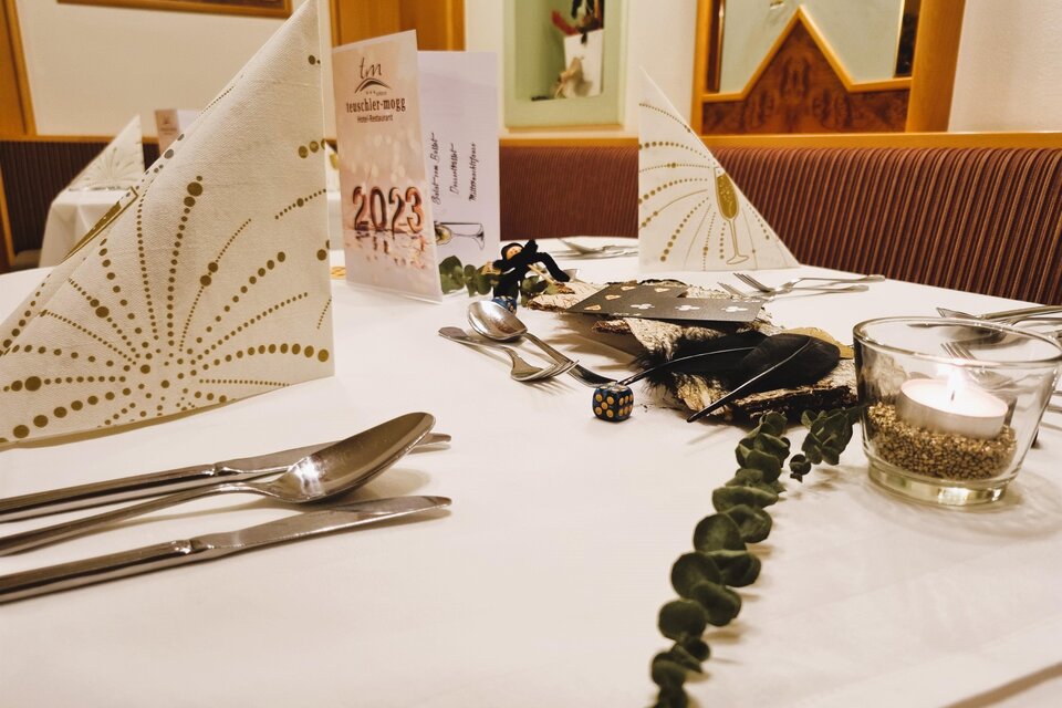Ein elegant gedeckter Tisch mit festlicher Dekoration und Kerzenlicht. Die Servietten sind kunstvoll gefaltet und es gibt Accessoires für eine besondere Veranstaltung. | © Teuschler-Mogg