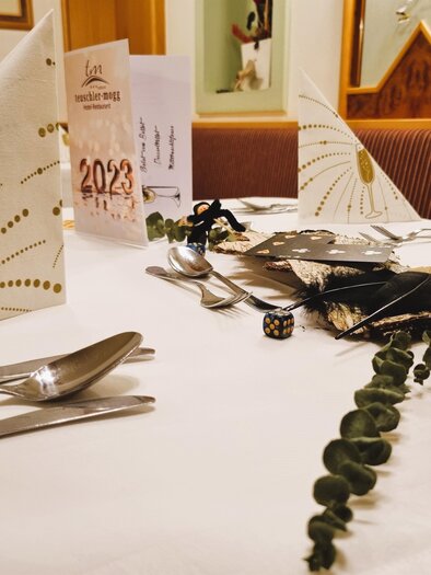 Ein elegant gedeckter Tisch mit festlicher Dekoration und Kerzenlicht. Die Servietten sind kunstvoll gefaltet und es gibt Accessoires für eine besondere Veranstaltung. | © Teuschler-Mogg