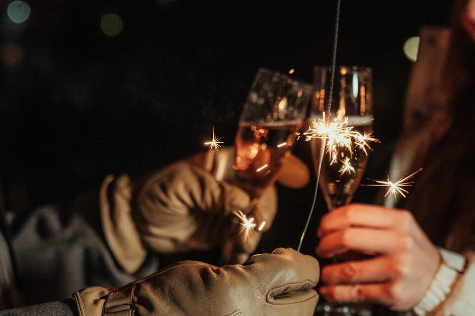 Zwei Personen stoßen mit Champagnergläsern an, während Funken sprühen. Die Szene ist festlich und feierlich. | © Region Graz-studio draussen