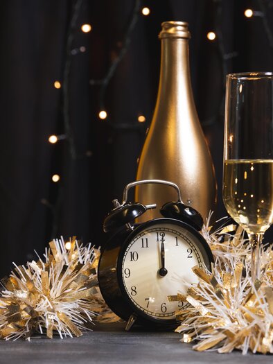 A golden champagne bottle stands next to two glasses and a clock. Festive decorations with lights and decorative ribbons create a cheerful atmosphere. | © Kirchenwirt Durlacher_Oststeiermark