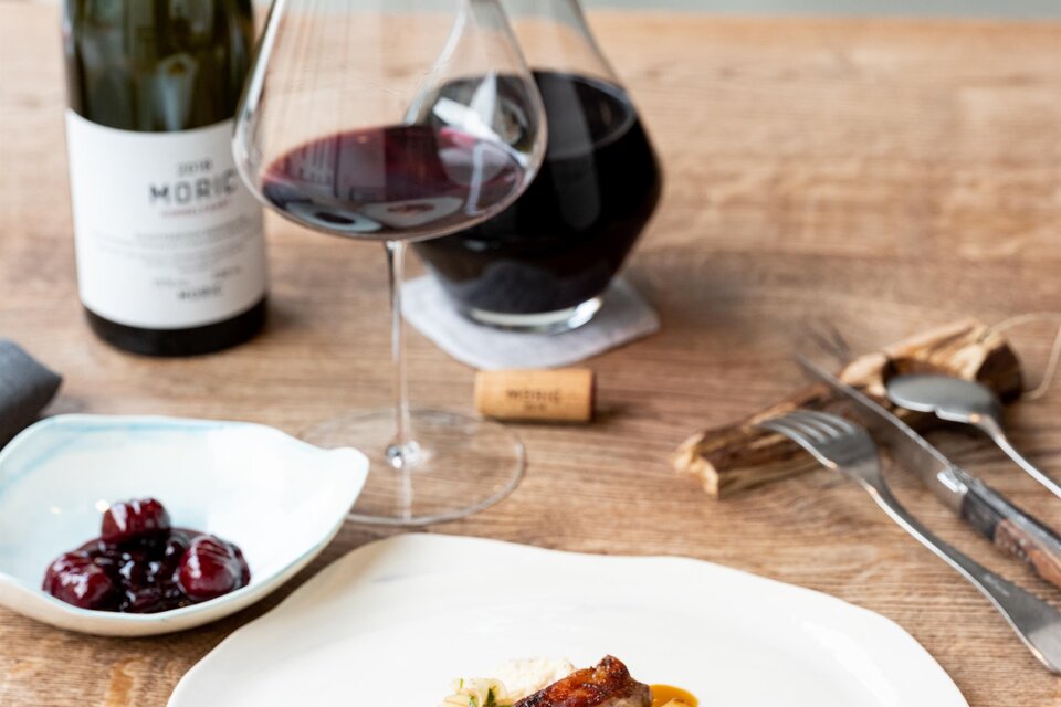 Ein elegantes Gericht mit Fleisch, Beilagen und Sauce auf einem weißen Teller. Dazu ein Glas Rotwein und eine Karaffe, begleitet von einer kleinen Schale mit Oliven. | © Michael Reidinger