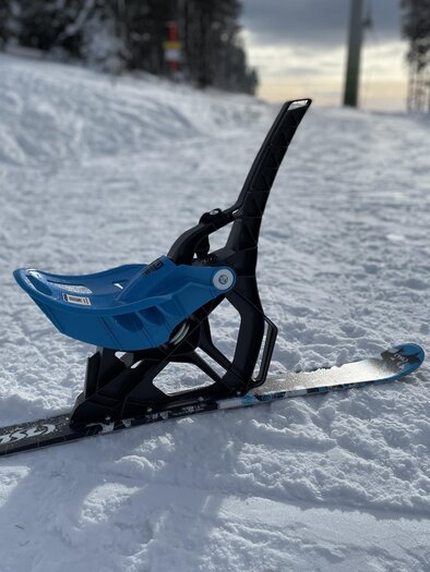 A blue sled stands on the snowy slope. In the background, snow-covered trees are visible. | © Steirisch Wandern