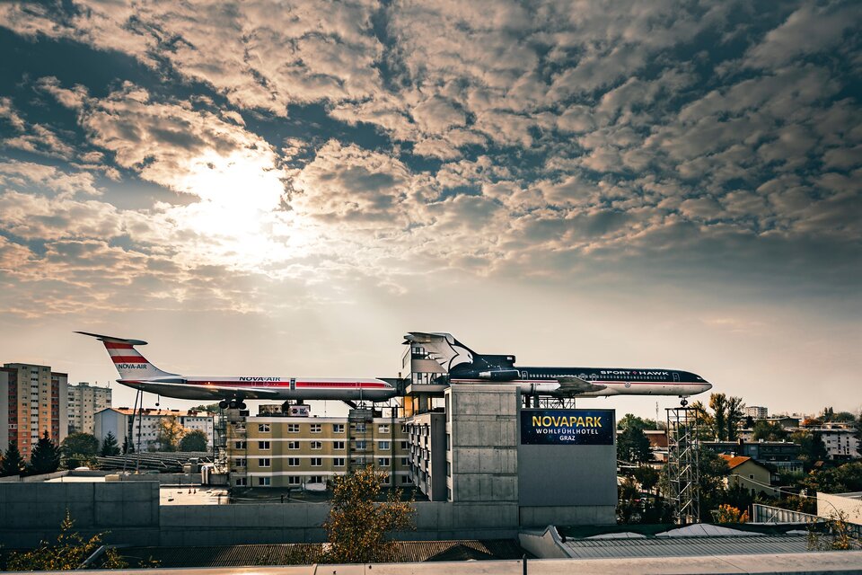 Ein ungewöhnliches Gebäude, das wie ein Flugzeug aussieht, steht auf einem Haus. Der Himmel ist bewölkt und es gibt eine stimmungsvolle Atmosphäre. | © (c)Ulrike_Rauch.jpg
