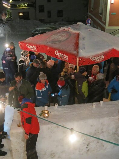 A large crowd gathers under a red sunshade in the snow. The scene takes place at night in a winter setting. | © Bergrettung