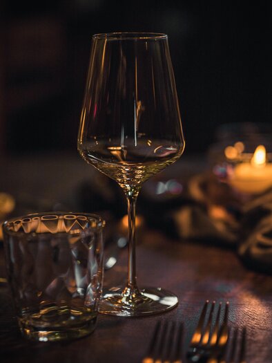 An elegant wine and water glass are on a beautifully set table. The room is softly lit, creating a cozy atmosphere. | © Das Ursprung