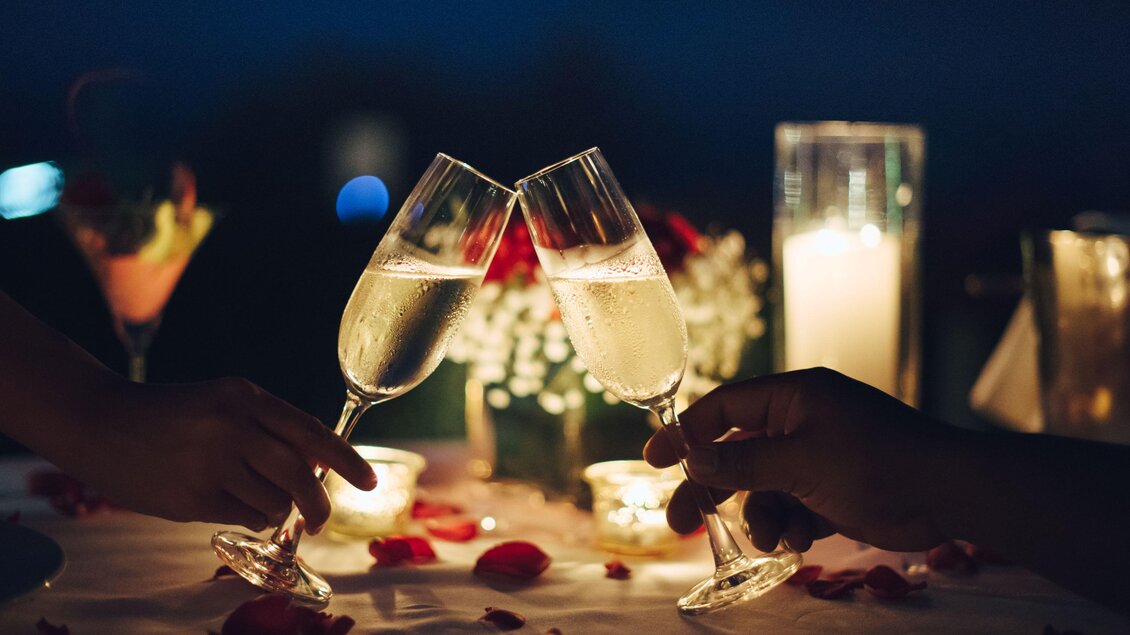 Ein romantisches Dinner bei Nacht mit zwei anstoßenden Gläsern Sekt. Der Tisch ist mit Rosenblüten und Kerzen dekoriert. | © TV Südsteiermark