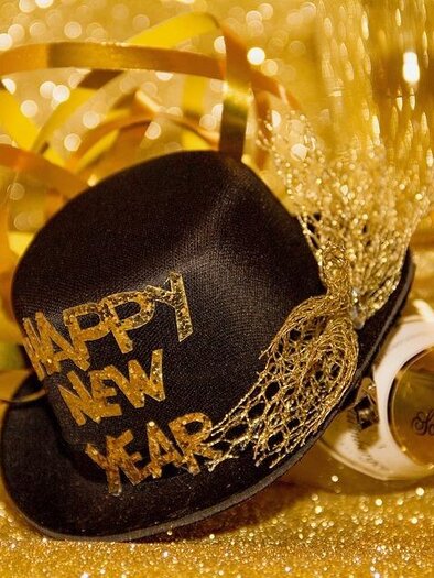 Ein festlicher Hut mit der Aufschrift „Happy New Year“ und eine Flasche Sekt liegen auf goldenem Glitzer. Dazu gibt es bunte Dekorationen und eine fröhliche Stimmung. | © Pixabay