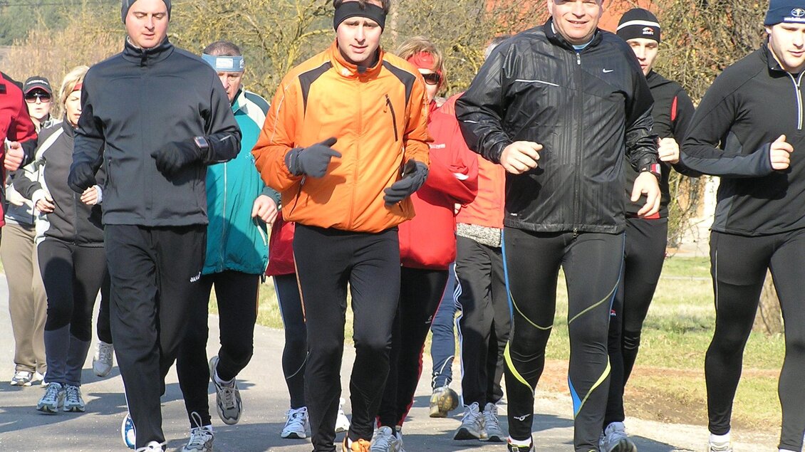 Eine Gruppe von Joggern läuft auf einer ruhigen Straße. Es sind verschiedene Laufbekleidungen zu sehen und die Teilnehmer sind motiviert.