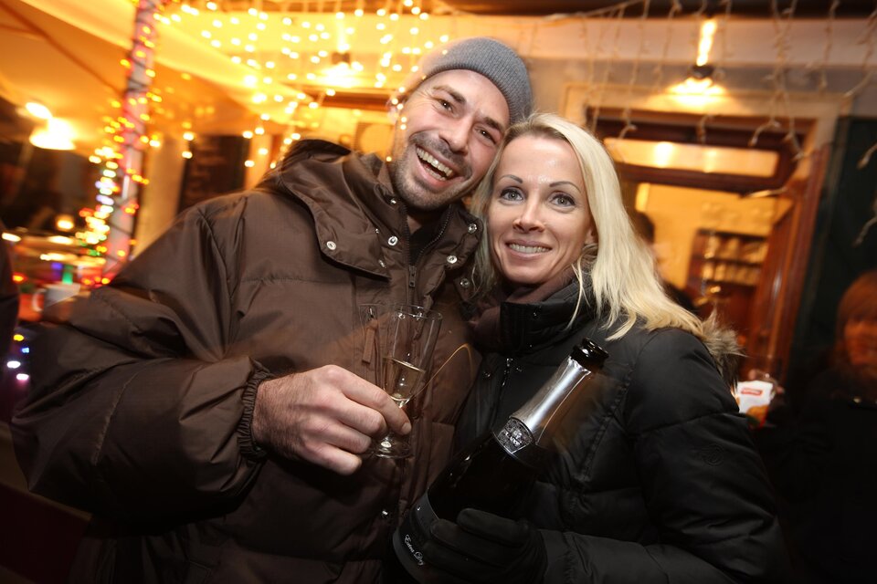 Ein fröhliches Paar posiert in einer festlich dekorierten Umgebung. Sie halten Gläser in der Hand und lächeln in die Kamera. | © graz-tourismus---harry-schiffer
