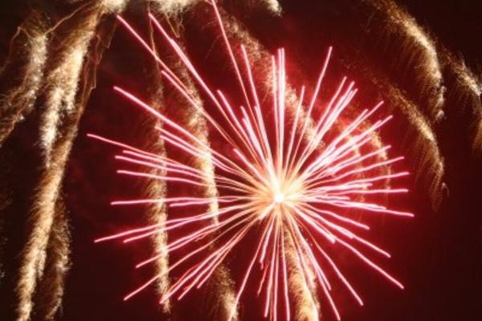 Ein Feuerwerk mit leuchtenden roten und goldenen Strahlen erhellt den Nachthimmel. Die Knaller bilden ein eindrucksvolles, symmetrisches Muster. | © Lederer