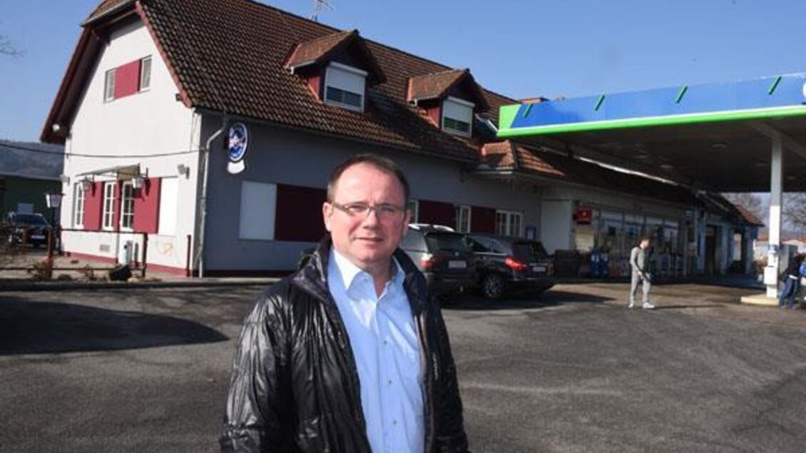 Ein Mann steht vor einer Tankstelle mit einem großen Gebäude im Hintergrund. Es ist ein klarer Tag und die Umgebung wirkt freundlich und einladend. | © Riedenbauer