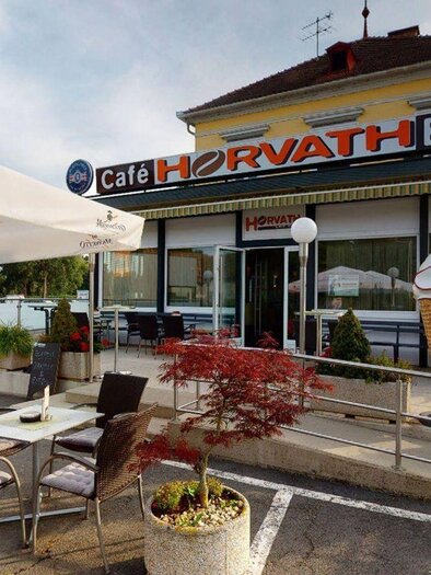 A cozy café with outdoor tables and a large ice cream sundae symbol. The entrance is welcoming, and the ambiance exudes a relaxed atmosphere. | © Cafe Horvath