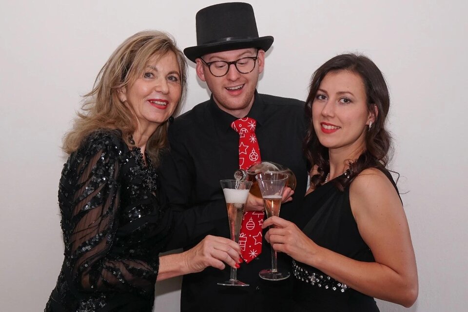 Drei Personen feiern zusammen und stoßen mit Gläsern an. Sie tragen festliche Kleidung und lächeln fröhlich. | © Philipp Fink