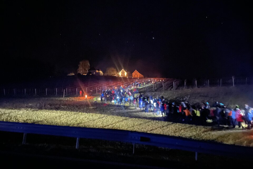 Eine große Gruppe von Menschen wandert bei Nacht entlang eines Feldes. Im Hintergrund sind beleuchtete Häuser zu sehen. | © Hannes Kofler