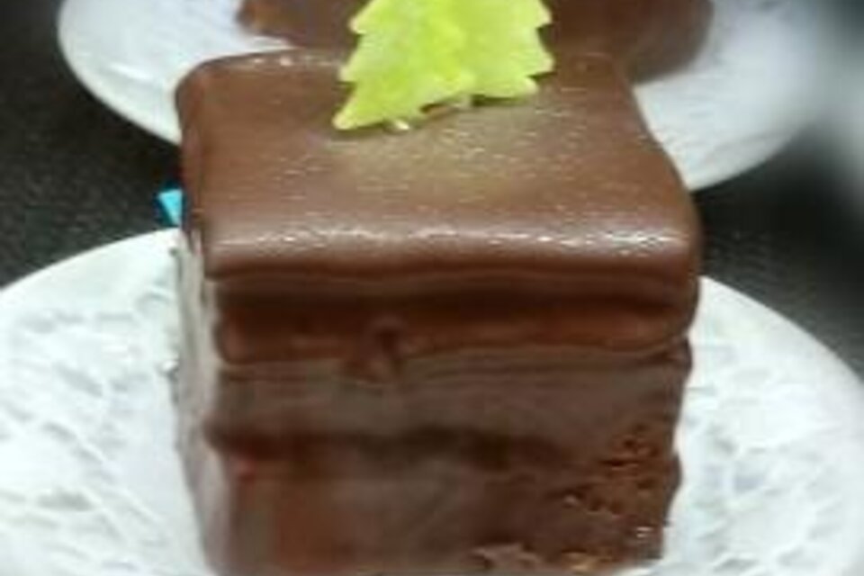 Ein quadratisches Schokoladengebäck auf einem weißen Teller. Oben ist es mit einem kleinen grünen Tannenbaum dekoriert. | © Café Idylle