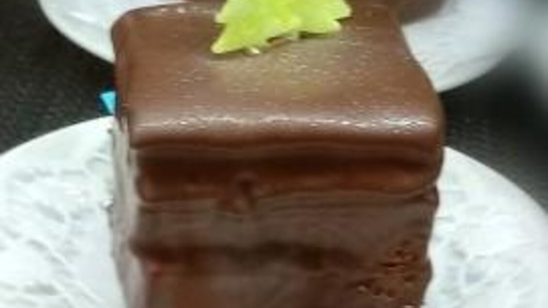 Ein quadratisches Schokoladengebäck auf einem weißen Teller. Oben ist es mit einem kleinen grünen Tannenbaum dekoriert. | © Café Idylle