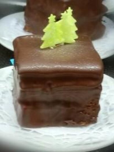 Ein quadratisches Schokoladengebäck auf einem weißen Teller. Oben ist es mit einem kleinen grünen Tannenbaum dekoriert. | © Café Idylle