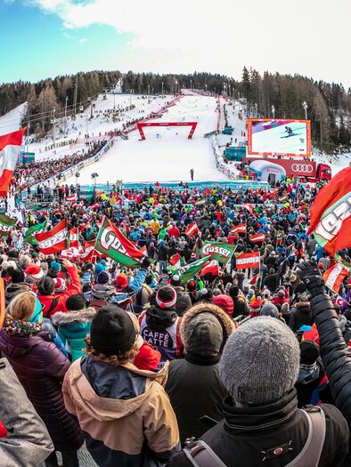 A large crowd cheers at a ski sporting event. Many spectators hold flags and celebrate in a festive atmosphere. | © Weltcup OK Semmering