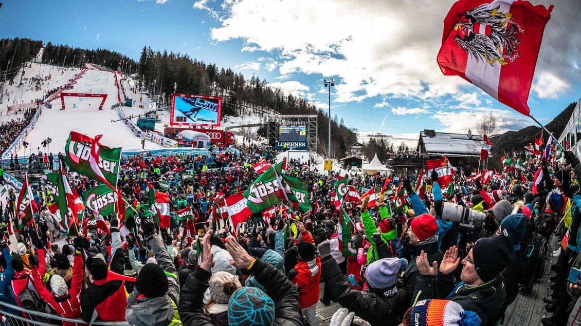 Eine große Menschenmenge feuert leidenschaftlich bei einem Ski-Event an. Viele Menschen halten Fahnen und zeigen ihre Unterstützung. | © Weltcup OK Semmering