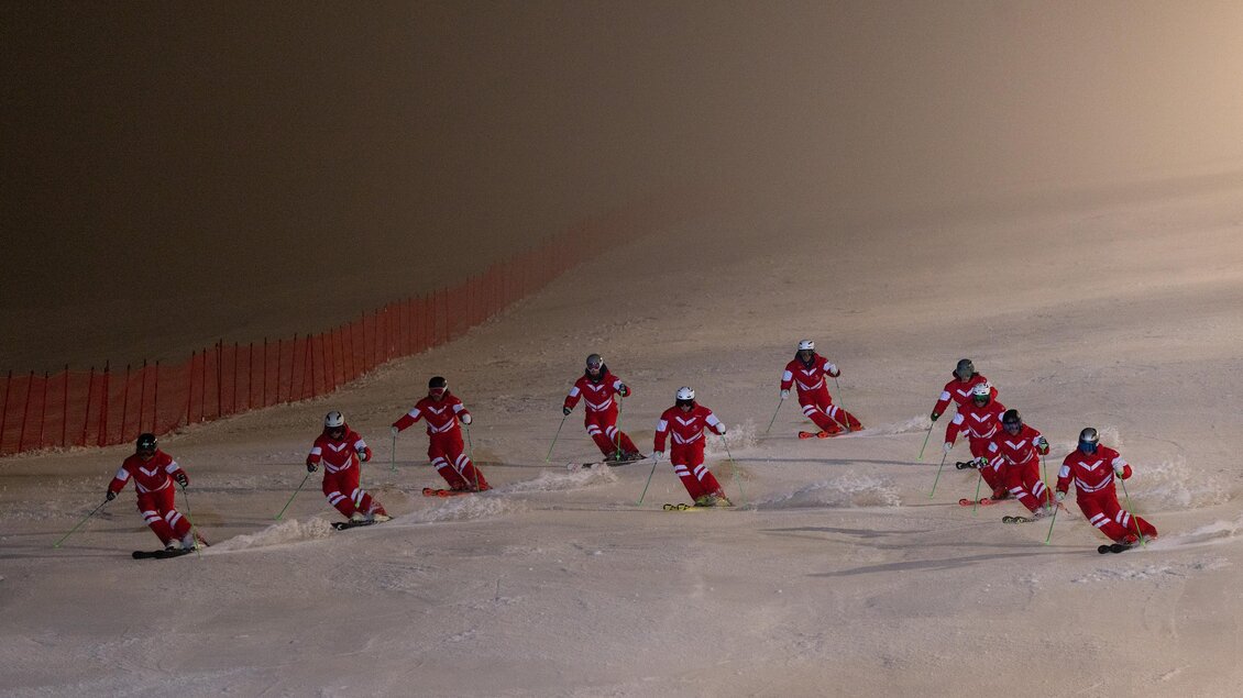 Eine Gruppe von Skifahrern in roten Anzügen fährt auf einer verschneiten Piste. Die Sicht ist aufgrund des Nebels eingeschränkt. | © Hans-Peter Steiner