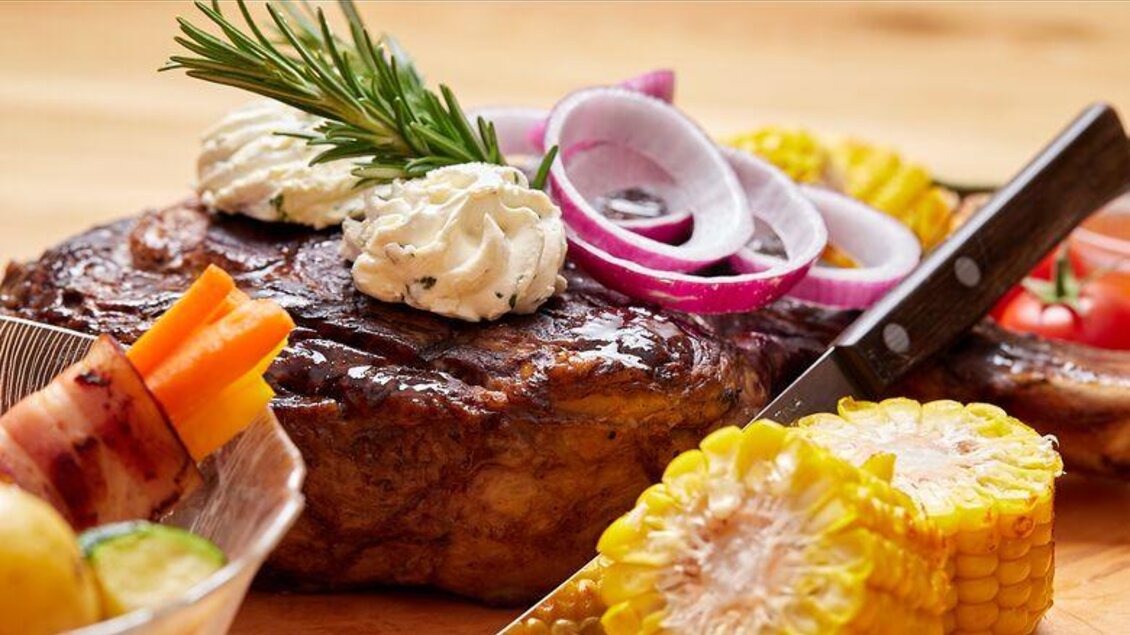Ein saftiges Steak mit Kräuterbutter und roten Zwiebeln. Dazu frisches Gemüse und eine Kürbiskern-Kolbe. | © Hauser Kaibling