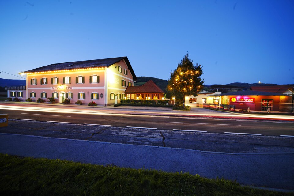 Ein gemütliches Hotel bei Dämmerung mit beleuchteten Fenstern. Im Vordergrund ist eine Straße mit vorbeifahrenden Autos zu sehen. | © Thomas Heschl