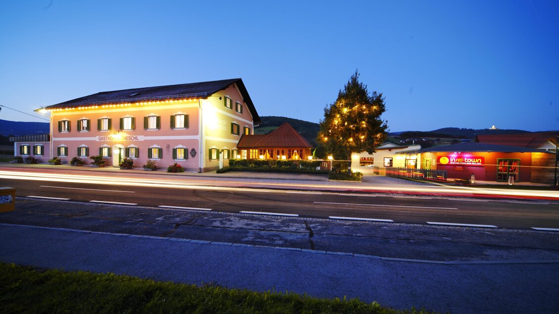 Ein gemütliches Hotel bei Dämmerung mit beleuchteten Fenstern. Im Vordergrund ist eine Straße mit vorbeifahrenden Autos zu sehen. | © Thomas Heschl