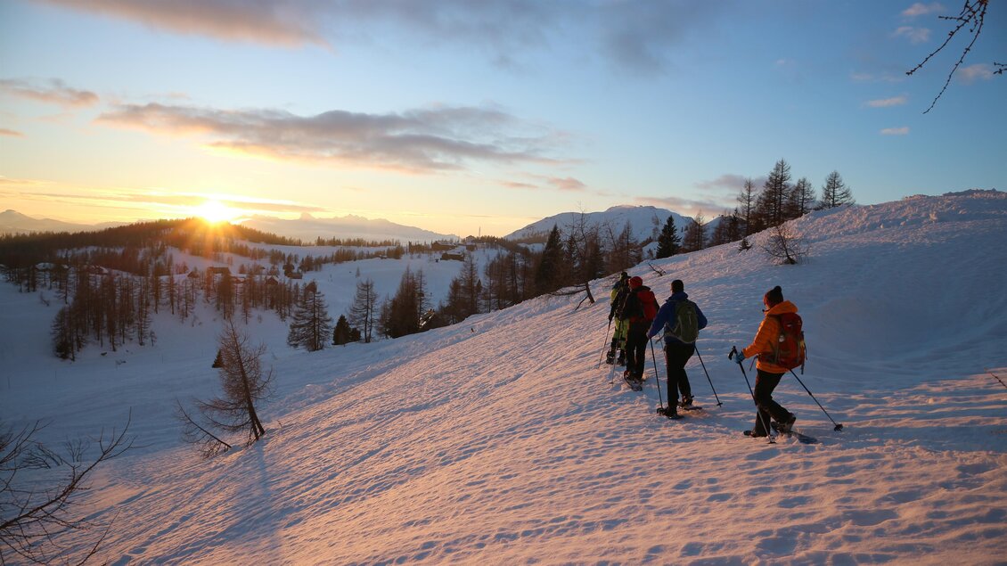 Eine Gruppe von Skifahrern wandert im Schnee bei Sonnenuntergang. Die verschneite Landschaft ist von Bäumen und Bergen umgeben. | © steirischwandern.at