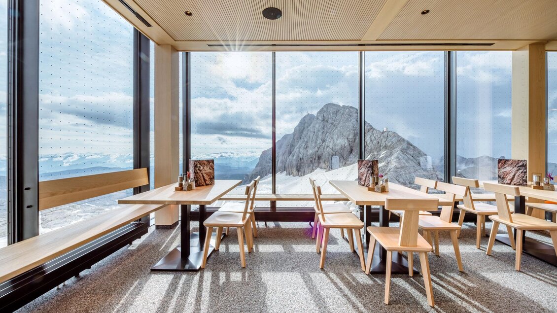 Ein modernes Restaurant mit großen Fenstern, das einen herrlichen Blick auf einen Berg bietet. Die Einrichtung besteht aus hellen Holzmöbeln und schafft eine einladende Atmosphäre. | © Christoph Huber