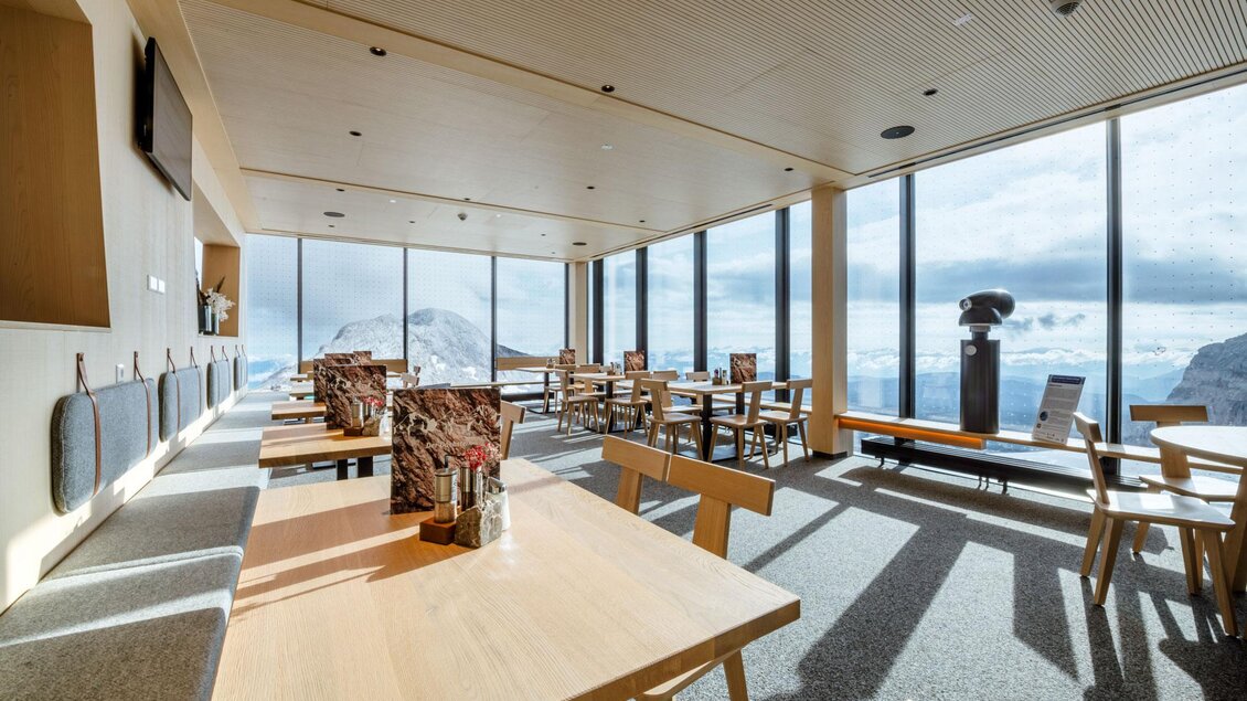 Ein modernes Restaurant mit großen Fenstern und Blick auf die Berge. Es gibt helle Holztische und stimmungsvolles Licht. | © Christoph Huber