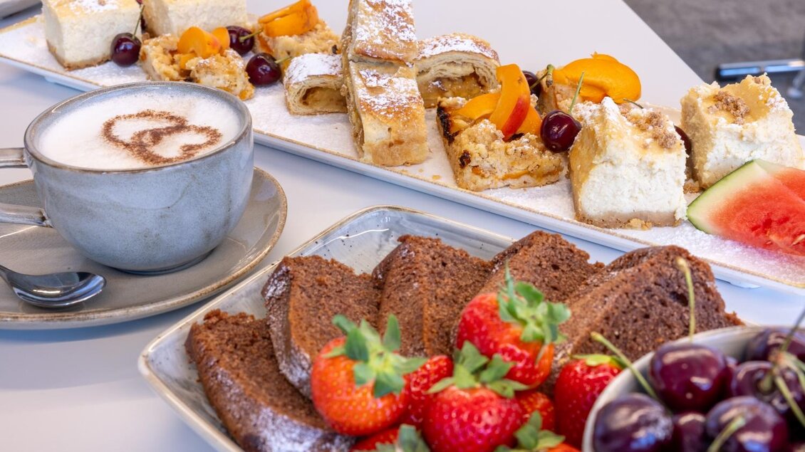Ein attraktives Desserttablett mit verschiedenen Süßigkeiten, darunter Kuchen, Obst und eine Tasse Cappuccino. Die Farben und die Vielfalt der Speisen laden zum Genießen ein. | © Harald Steiner