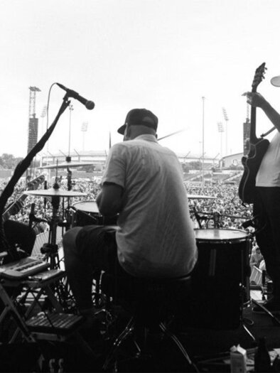 A band is playing on a stage in front of a large, enthusiastic audience. In the background, there are more stages and a ferris wheel visible. | © Ingo Pertramer