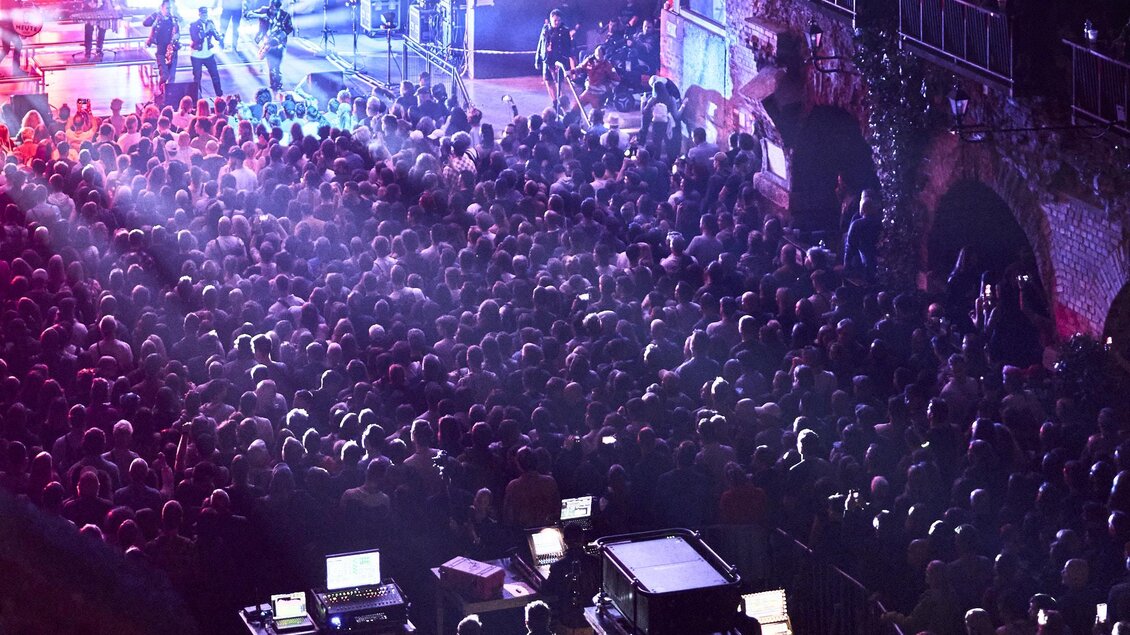 Ein lebhaftes Konzert mit einer großen Menschenmenge unter bunten Lichtern. Die Atmosphäre ist energetisch und feierlich. | © Stefan Leitner