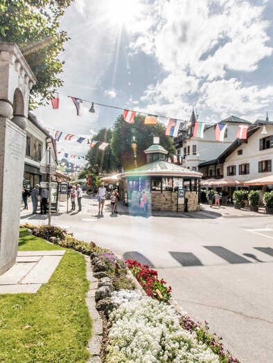 A lively street with flower beds and colorful flags. People stroll in a picturesque village with charming buildings. | © Gerhard Pilz/Gerhard Pilz - www.gpic.at