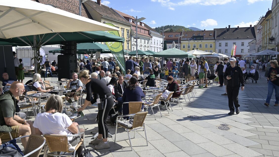 Ein belebter Platz mit vielen Menschen und Tischen im Freien. Sonnenschein und Markisen schaffen eine angenehme Atmosphäre. | © Norbert Ortner