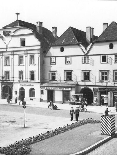A historic town square with old buildings and a small plaza. Vehicles and pedestrians are visible, highlighting the lively atmosphere of the scene. | ©  MuseumsCenter Leoben