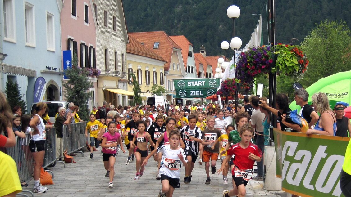 Eine Gruppe von Kindern läuft ein Rennen auf einer Straße in einer Stadt. Im Hintergrund sind bunte Häuser und Zuschauer zu sehen. | © Foto Ullrich