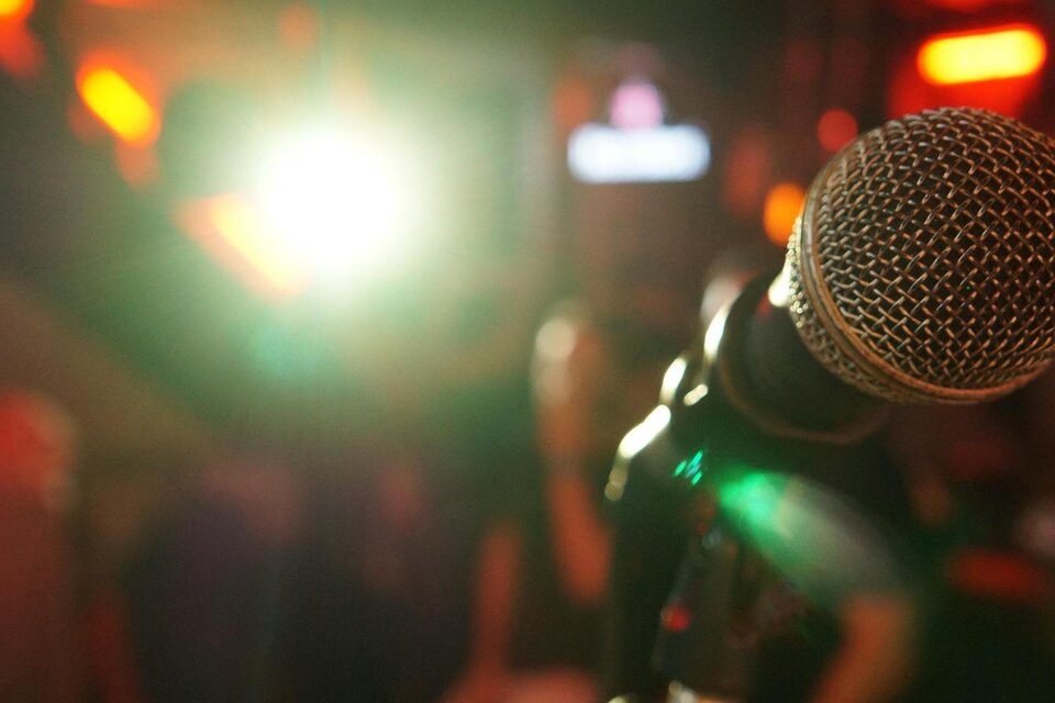 Mikrofon im Vordergrund mit verschwommenem Hintergrund. Die Szene ist beleuchtet mit bunten Lichtern, die eine lebhafte Atmosphäre schaffen. | © Pixabay