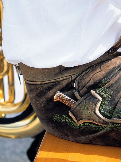Ein Teil eines traditionellen bayerischen Outfits mit schönen Lederhosen ist zu sehen. Im Hintergrund steht eine glänzende Tuba. | © Steiermark Tourismus