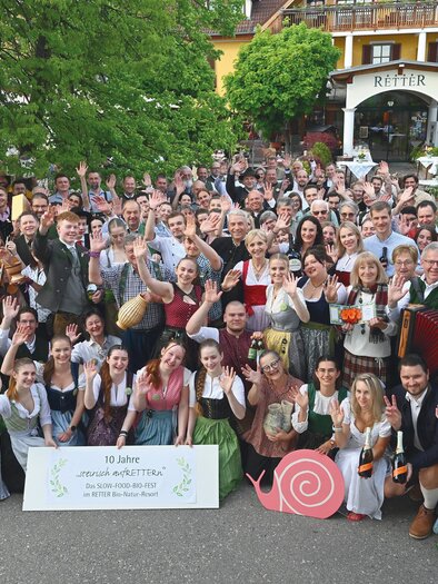 A large group of people in traditional clothing poses happily outdoors. In the background, trees and a building are visible. | © RETTER- BIO- Natur-Resort