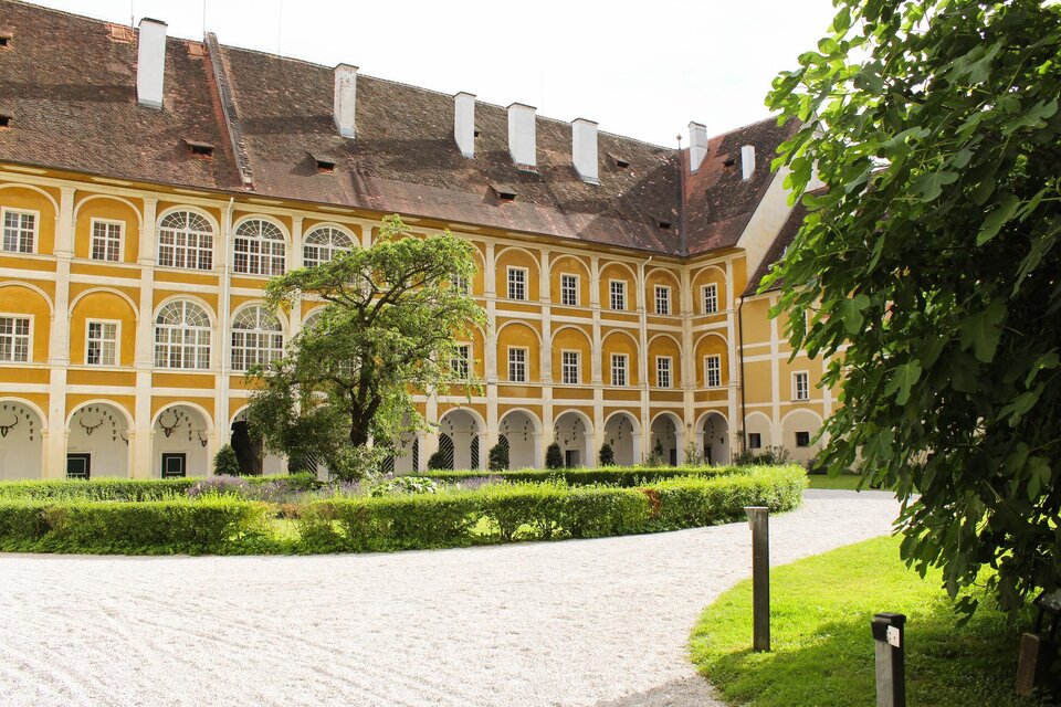 Ein historisches Gebäude mit gelber Fassade und großen Fenstern. Im Vordergrund befinden sich ein gepflegter Garten und ein gepflasterter Weg. | © TV Südsteiermark - Irene Löschnig