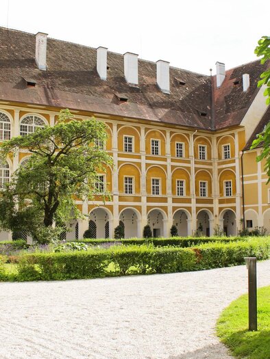 A historical building with a yellow facade and large windows. In the foreground, there is a well-kept garden and a paved path. | © TV Südsteiermark - Irene Löschnig